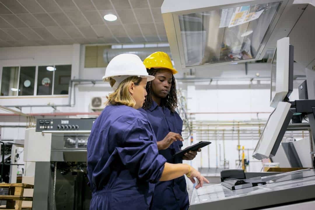 clm_feminino-funcionário-industrial-ensinando-colega-operar-máquina-apontando-placa-de-controle-usando-tablet